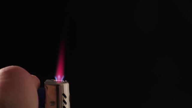 Igniting turbo lighter on black background, closeup. Burning flame on black background