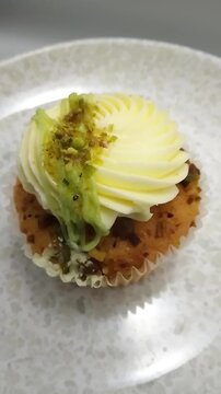 Cupcake Drizzled with Pistachio Cream and Topped with Crushed Pistachio on Plate Viewed from Above while Spinning, Close up Vertical Video