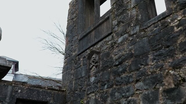 Close-up of the ancient limestone wall and decorative window frame of the Lynch Memorial building on a grey, overcast day in Galway