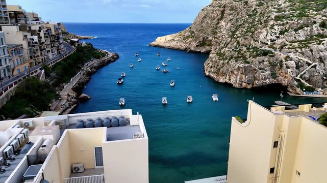 High Angle View of Scenic Xlendi Bay During a Bright Summer Day in Gozo Malta Showing Traditional Boats Moored in Turquoise Mediterranean Waters Surrounded by Steep Limestone Cliffs and Local Building