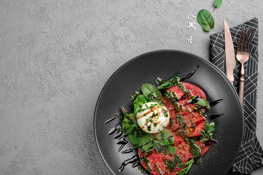 Fresh tomato carpaccio with creamy burrata, pesto drizzle, fresh basil leaves and balsamic glaze on black plate. Elegant Italian appetizer, gourmet salad-style dish, restaurant presentation, top view