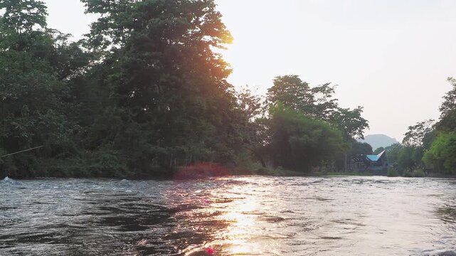 Beautiful river landscape at sunset with lush green trees and golden sunlight reflecting on the water surface. Khlong Wang Takhrai, Nakhon Nayok, Thailand