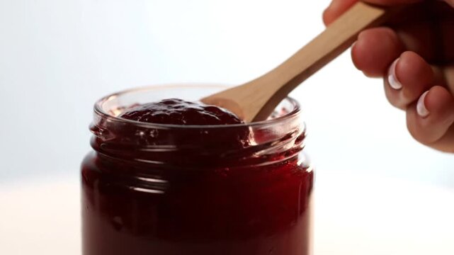 Spoon stirs fruit jam in jar with close up.