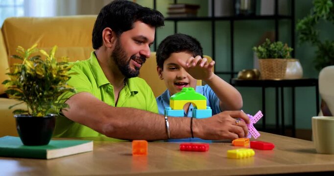Indian asian young father son building toy windmill together in playful atmosphere, creating colorful plastic tower while spending quality family time in modern living room at home