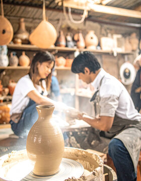 Warm atmosphere of a pottery workshop with blurred background, showcasing friends working together to shape clay on a wheel