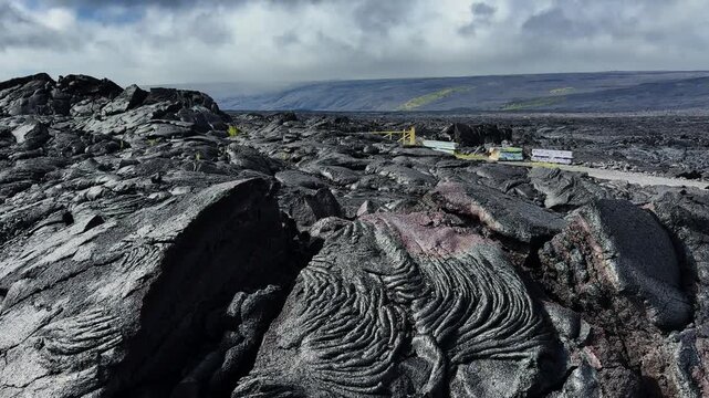Static shot of black solidified lava flows with volcanic textures under a cloudy sky.