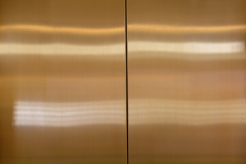 The shiny gold metal wall is reflective and has a smooth texture. the stainless steel background of elevator door. © Rattanachat