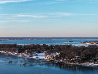 Obraz premium Long island sound shoreline with snow covered trees and frozen water near port washington, new york featuring a distant cityscape horizon on a clear winter day