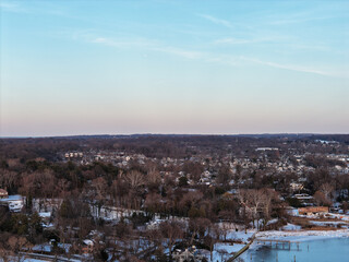 Obraz premium Aerial view displaying a peaceful winter landscape over port washington, new york, with suburban homes nestled among bare trees and snow lining the waterfront along plum beach point drive