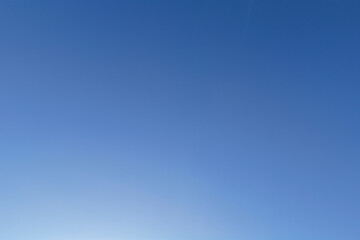 Fototapeta premium Undisturbed expanse of a clear blue sky, presenting a gradient from lighter to deeper blue, with a wispy vapor trail visible in the upper right, offering ample copy space