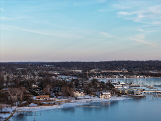 Port washington coastline in nassau county, new york, featuring snow covered landscapes, residential buildings, and a marina with docked boats along the partially iced bay during winter