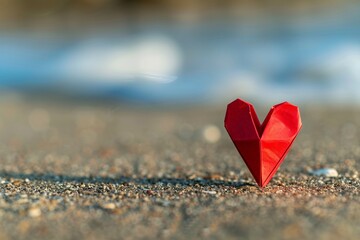 Fototapeta premium Small red paper heart standing on sandy beach romantic love symbol with soft sunlight and ocean background