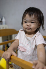 Cute baby girl holding crib railing while looking forward