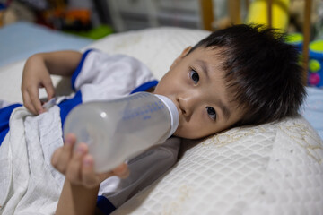 Little boy drinking milk from bottle lying on bed at home