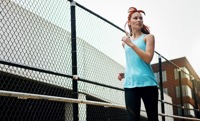 Obraz premium Earphones, running and woman in city for training, low angle or challenge for health benefits. Outdoor, person or runner with exercise, sound or practice with cardio, fitness or listening to playlist