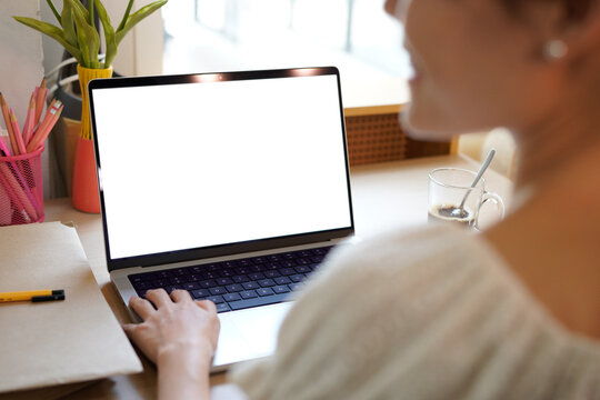 Back view mockup image of a woman working and typing on laptop computer with blank screen while sitting on a desk at home