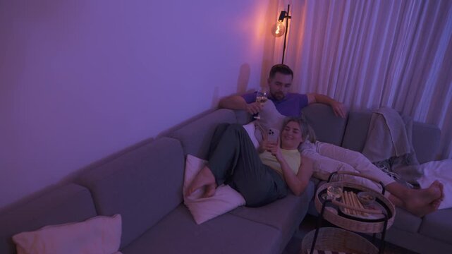 Couple Relaxing on Sofa at Night Using Smartphones with Snacks and Wine