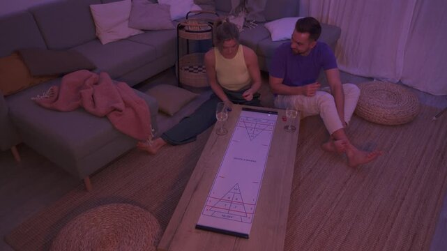 Couple Playing Table Shuffleboard at Home During Cozy Evening with Wine
