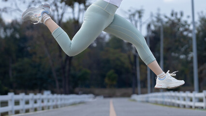 Woman jumping in mid-air while running outdoors on a road. Concept of fitness