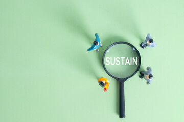 Miniature business people standing around magnifying glass focusing on the word Sustain on green background. Environmental sustainability, ESG, eco friendly business, and future plan concept.