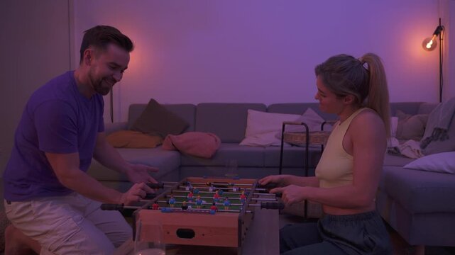 Happy Couple Playing Tabletop Foosball Together in Cozy Living Room