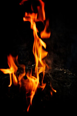 Fototapeta premium Tall vertical fire column on dark background, elegant dancing orange flames twisting upward like molten ribbons, intense heat and dramatic light