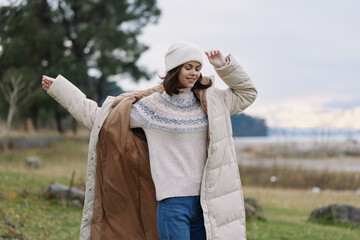 Woman wearing a long beige puffer coat and knit sweater outdoors, enjoying a windy day by the...