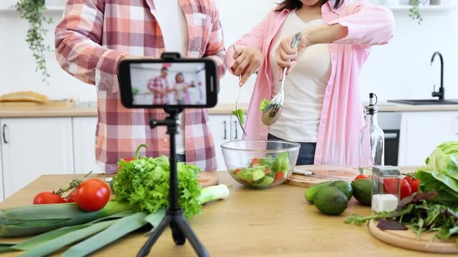 A couple is filming a cooking vlog in their kitchen, preparing a healthy salad with fresh vegetables