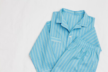 Top view of blue green striped pajama suit on white bed. Minimal style, cozy, comfort pyjamas. Sleepwear fashion concepts, self-care, wellness, calm lifestyle, home aesthetics, morning routines