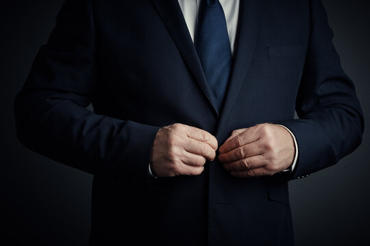 Hands, businessman and button jacket in studio for getting ready, corporate style and professional. Dressing, person and fasten suit on black background for work preparation, formal fashion or classy