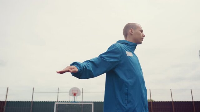 closeup training white male balancing ball on urban court, soft light and highrise skyline, arms extended in deliberate motion, precise touch and composure, composed performer demonstrating finesse