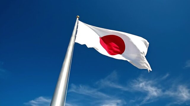 The Japanese flag waving on a silver pole against a clear blue sky with wispy clouds