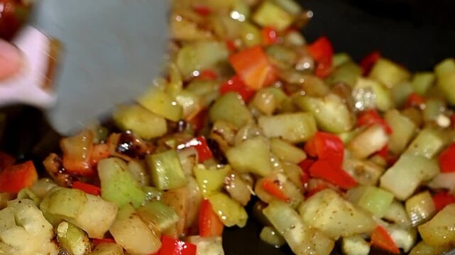 Colorful vegetable stew cooking slowly in a stainless steel pan. Zucchini rounds, bell pepper strips, carrot slices and onion chunks simmering in their own juice with herbs. Steam rising, gentle bubbl