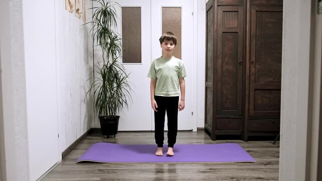 Boy doing exercise lifting on toes standing on yoga mat. Home workout concept. Schoolboy does calf raises during morning workout routine. Sporty lifestyle. High quality 4k footage.