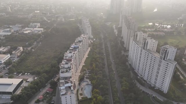 Aerial view of Swarn Nagri Road with tall residential towers and a tree-lined boulevard, seen under light haze from air pollution, reflecting both planned urban growth and environmental challenges