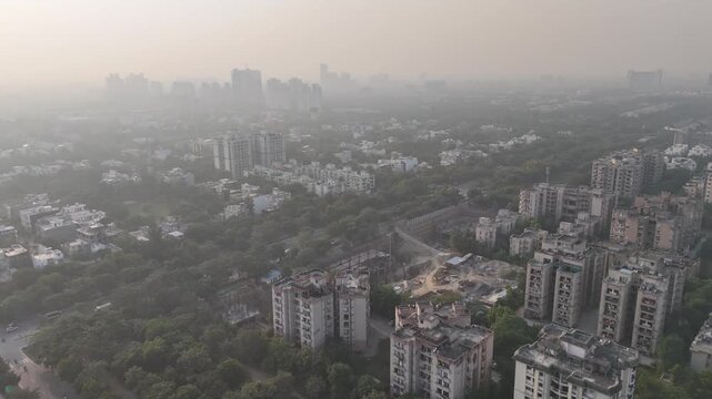 Top-down aerial footage of a landscaped roundabout with moving vehicles, canals, and dense greenery, softened by atmospheric haze that reveals ongoing air pollution in the urban skyline.