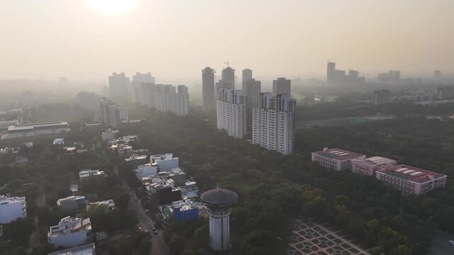 Wide aerial of Noida under a hazy sky, showing high-rises, housing clusters, and urban sprawl softened by air pollution that blurs the distant skyline.
