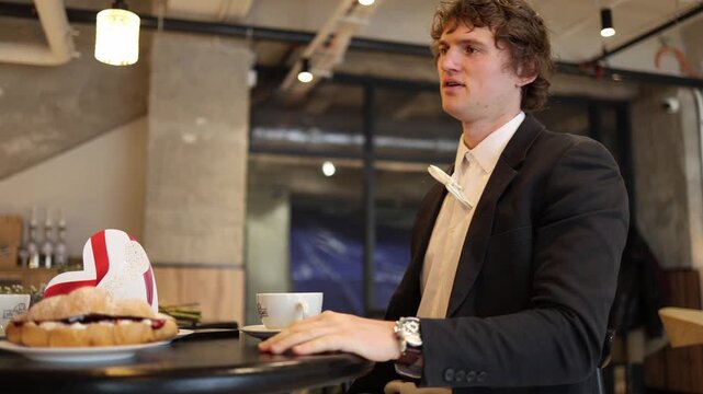 Guy sits confused adjusting his jacket while avoiding the topic that caused tension earlier creating an awkward quiet moment as the girl watches him trying to regain confidence at the table