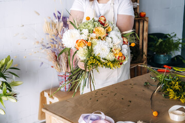 Florist presents completed flower bouquet over wooden workspace with ribbons and floral stems. Floral design masterclass, experiential retail, hands-on workshop