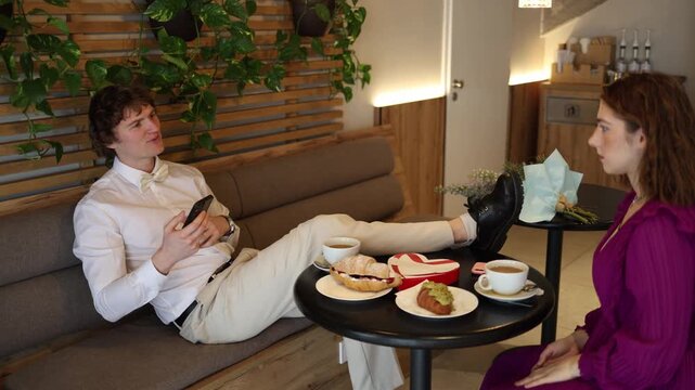 A guy puts his feet on the table and scrolls his phone ignoring the girl during their cafe date creating an awkward disrespectful moment as she sits confused and disappointed