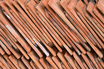 A close up diagonal view of numerous old terracotta clay roof tiles stacked neatly together showing weathered textures and natural earthy tones