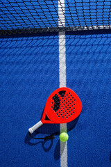 Padel tennis racket and ball on blue court with center line and net