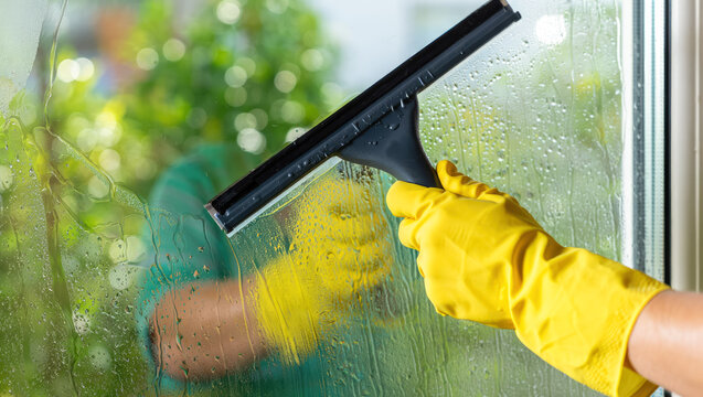 Gloved hand cleaning window with squeegee, removing water and dirt, outdoor setting, applicable for home maintenance material, cleaning services and household care, cleaning supplies, spring cleaning