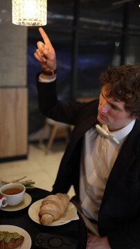 Vertical screen man sits at the cafe date looking unsteady and holding his chest showing he has clearly had too much to drink creating an awkward moment while the scene shifts into quiet concern