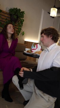 Vertical screen man kneels during cafe date doing whatever the woman asks showing obedient behavior playful dynamic humor and light tension in a scene of a boyfriend acting submissive