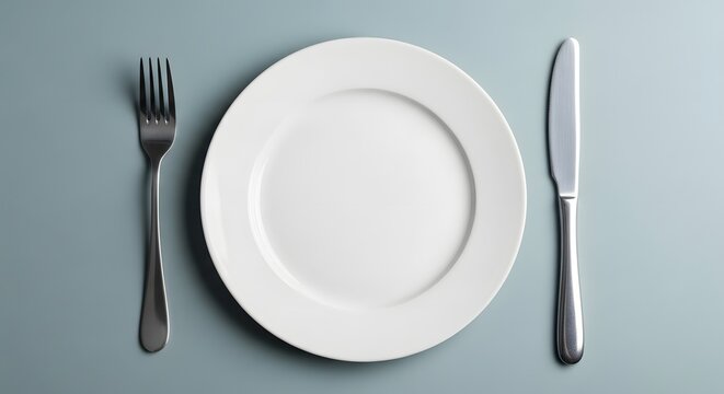 An empty white plate with a fork and knife on a table