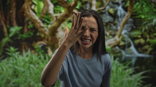 Woman with clenched fist thrust forward and hand near cheek in forest scene, closeup showing bare hand and face; anger defiance.