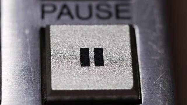 Macro close up of finger pressing silver pause button with black double bars