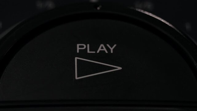 Finger presses circular play button with white triangle icon in dark setting