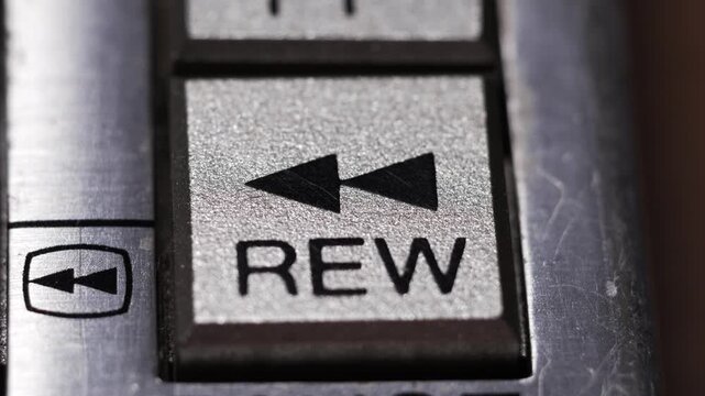 Macro close up of finger pressing silver rewind button with double triangle icon